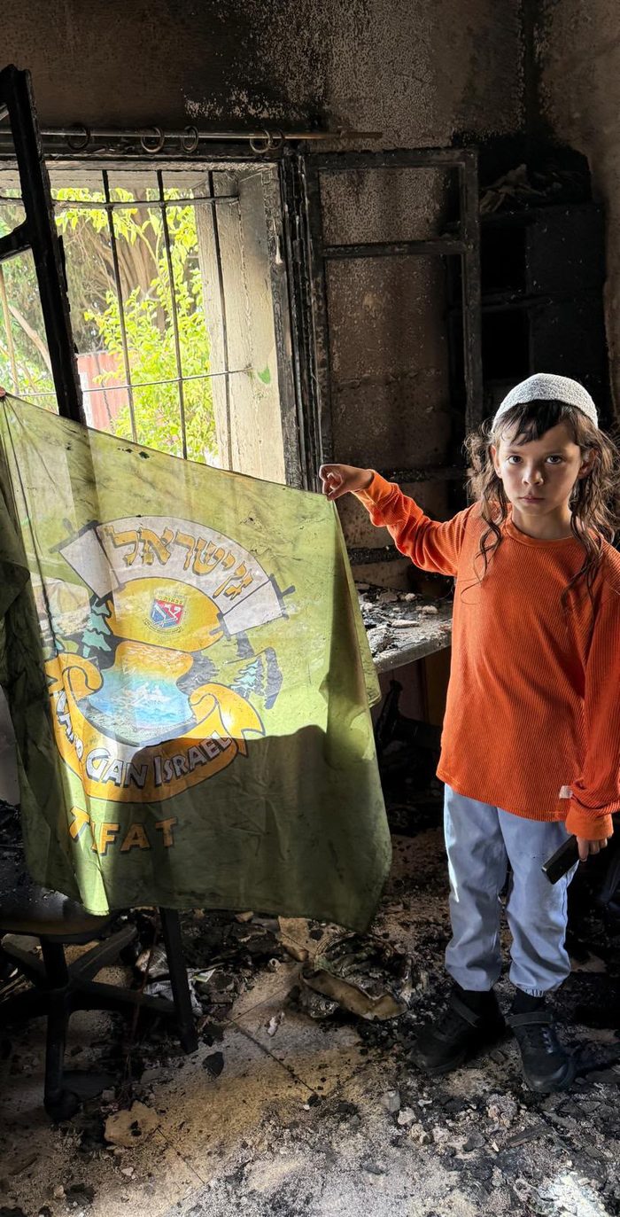 A young camper holds up the Camp Gan Israel Tzfat flag in a burnt room