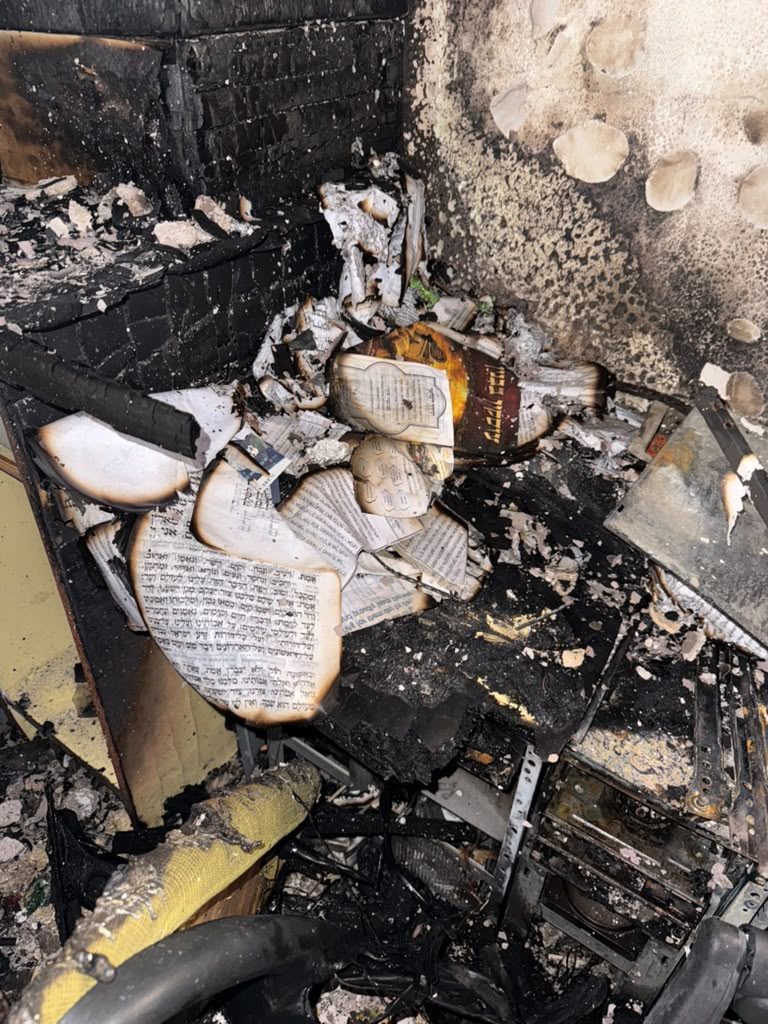 Charred pages of seforim in the ashes of a burnt shelf