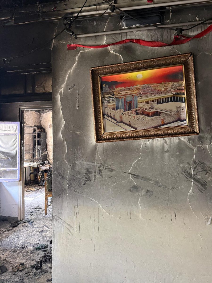 The framed picture of the Beis Hamikdash hanging on a soot-blackened, cracked wall inside the burnt camp building